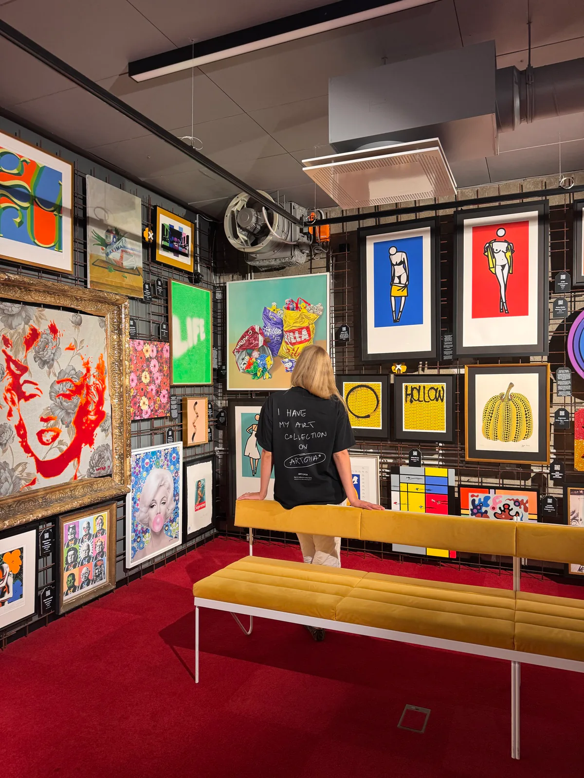 A visitor viewing a densely hung collection of colourful framed artworks.
