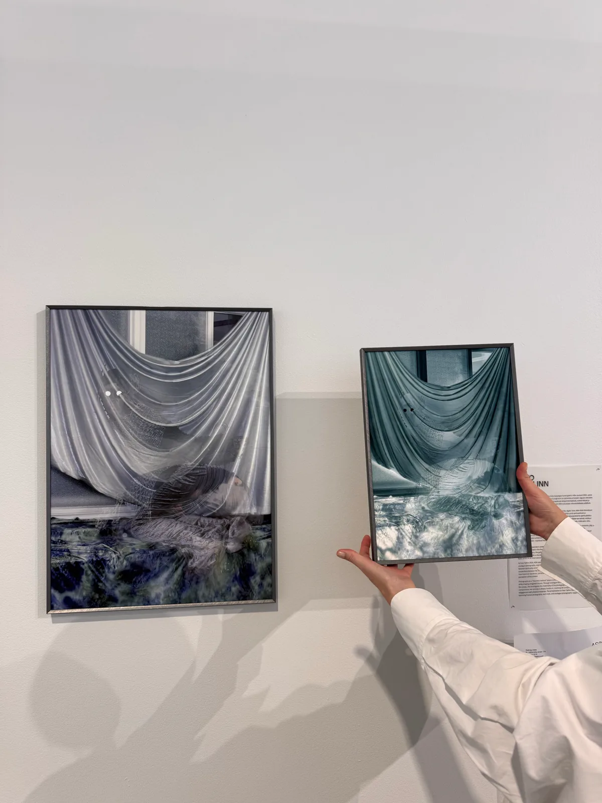 Two framed artworks, with a person holding one beside the other on a wall.